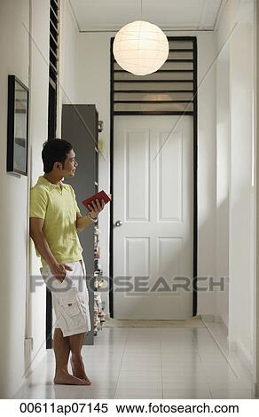 Man standing in hallway at home, holding a book, looking away View Large Photo Image Stock Photography - Man standing in hallway at home, holding a book, looking away. Fotosearch