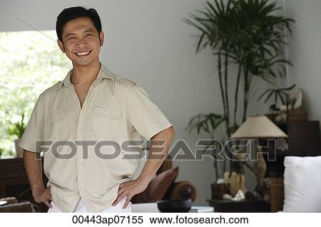 Man standing in living room, hands on hips, smiling View Large Photo Image Stock Photography - Man standing in living room, hands on hips, smiling. Fotosearch