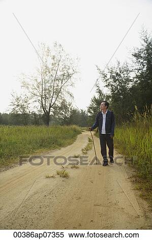 Stock Photography - Man walking down dirt road, hiking. Fotosearch