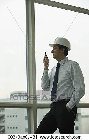 man wearing hard hat, talking into walkie talkie and looking out window View Large Photo Image Stock Image - man wearing hard hat, talking into walkie talkie and looking out window. Fotosearch