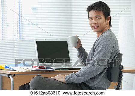 Man with cup relaxing at desk and looking at camera View Large Photo Image Stock Image - Man with cup relaxing at desk and looking at camera. Fotosearch