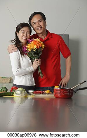 Mature couple in kitchen, embracing, woman holding bouquet of flowers View Large Photo Image Stock Photo - Mature couple in kitchen, embracing, woman holding bouquet of flowers. Fotosearch