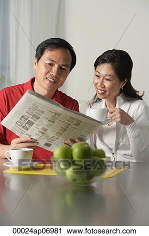 Stock Image - Mature couple looking at newspaper and having coffee. Fotosearch