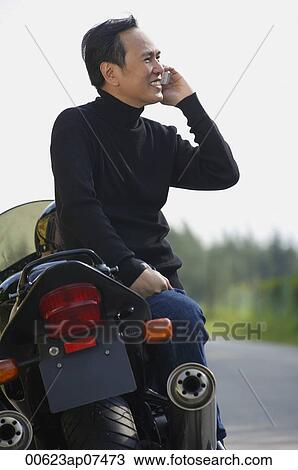 Mature man leaning on motorcycle, talking on mobile phone View Large Photo Image Stock Image - Mature man leaning on motorcycle, talking on mobile phone. Fotosearch