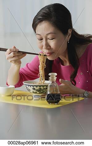 Stock Image - Mature woman eating a bowl of noodles, eyes closed. Fotosearch