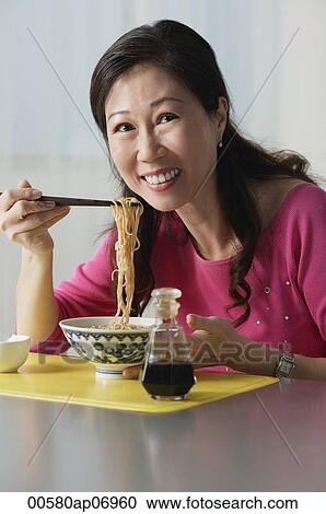 Stock Image - Mature woman eating a bowl of noodles. Fotosearch