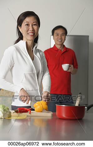 Stock Image - Mature woman in kitchen preparing a meal, man standing behind her, both looking at camera. Fotosearch