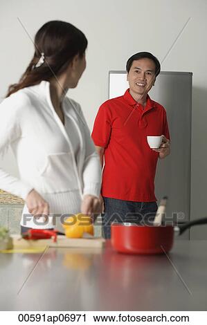 Stock Image - Mature woman in kitchen preparing a meal, turning to look man standing behind her. Fotosearch