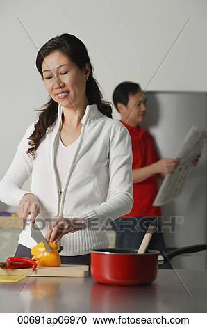 Mature woman in kitchen preparing a meal, man in background holding newspaper View Large Photo Image Stock Image - Mature woman in kitchen preparing a meal, man in background holding newspaper. Fotosearch
