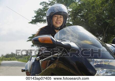 Stock Photography - Mature woman riding motorcycle and wearing helmet. Fotosearch