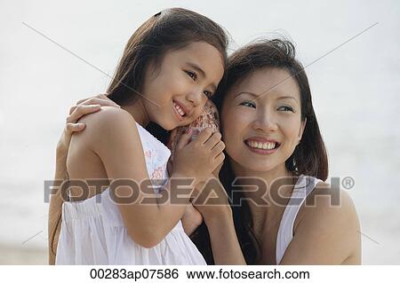 Mother and daughter on beach with ears up to a conk shell, listening to the ocean View Large Photo Image Stock Photograph - Mother and daughter on beach with ears up to a conk shell, listening to the ocean. Fotosearch