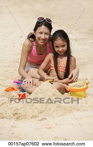 Mother and daughter sitting in sand on beach, building sand castle View Large Photo Image Stock Image - Mother and daughter sitting in sand on beach, building sand castle. Fotosearch