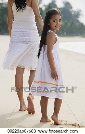 Mother and daughter walking down beach, daughter looking back towards camera smiling View Large Photo Image Stock Image - Mother and daughter walking down beach, daughter looking back towards camera smiling. Fotosearch
