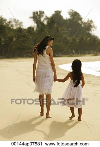 Mother and daughter walking hand and hand on beach, wearing white dresses View Large Photo Image Stock Image - Mother and daughter walking hand and hand on beach, wearing white dresses. Fotosearch