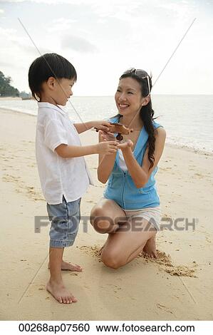 Stock Image - Mother and son on beach, boy holding wooden airplane. Fotosearch