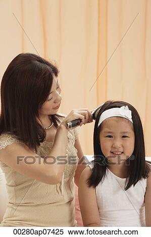Stock Photography - Mother brushing daughter's hair, young girl looking at camera, smiling. Fotosearch