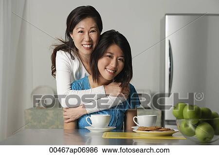 Stock Photograph - Mother embracing adult daughter, both smiling at camera. Fotosearch