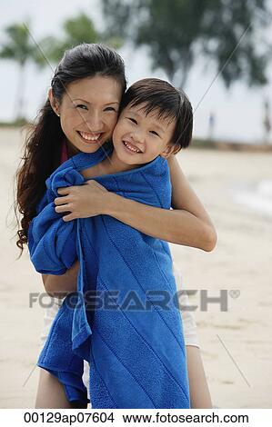 Mother hugging son on beach, son wrapped in blue towel View Large Photo Image Picture - Mother hugging son on beach, son wrapped in blue towel. Fotosearch