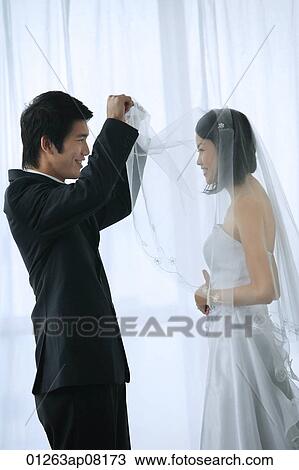 The groom lifts the brides veil to kiss her View Large Photo Image Stock Image - The groom lifts the brides veil to kiss her. Fotosearch