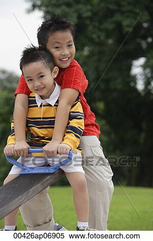 Two brothers sitting on See-Saw, smiling at camera View Large Photo Image Stock Photography - Two brothers sitting on See-Saw, smiling at camera. Fotosearch