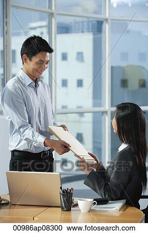 Two colleagues smile at each other as they exchange documents View Large Photo Image Stock Image - Two colleagues smile at each other as they exchange documents. Fotosearch