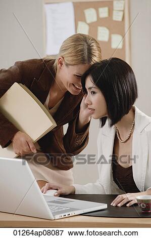 Two female colleagues smile and laugh together at work View Large Photo Image Stock Photo - Two female colleagues smile and laugh together at work. Fotosearch