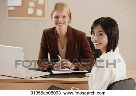 Two female colleagues smile at the camera together View Large Photo Image Stock Image - Two female colleagues smile at the camera together. Fotosearch