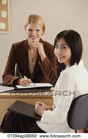 Two female colleagues smile at the camera together View Large Photo Image Stock Image - Two female colleagues smile at the camera together. Fotosearch