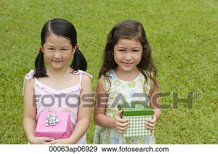 Two girls holding gift boxes, standing side by side, smiling at camera View Large Photo Image Stock Photo - Two girls holding gift boxes, standing side by side, smiling at camera. Fotosearch