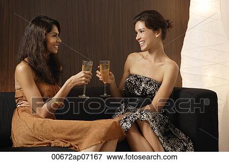 Two girls sitting on couch, toasting each other with champagne, smiling at each other View Large Photo Image Stock Photo - Two girls sitting on couch, toasting each other with champagne, smiling at each other. Fotosearch