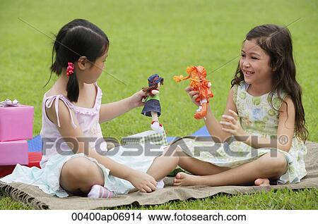 Two girls sitting on picnic blanket, playing with dolls View Large Photo Image Picture - Two girls sitting on picnic blanket, playing with dolls. Fotosearch