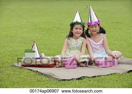 Two girls wearing party hats sitting on picnic blanket, surrounded by gifts View Large Photo Image Stock Photo - Two girls wearing party hats sitting on picnic blanket, surrounded by gifts. Fotosearch