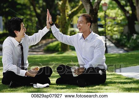 Two men eat their lunch together in the park and high five View Large Photo Image Stock Photo - Two men eat their lunch together in the park and high five. Fotosearch
