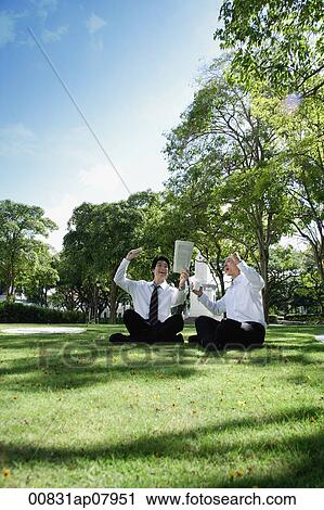 Two men get excited as they read the newspaper in the park View Large Photo Image Stock Image - Two men get excited as they read the newspaper in the park. Fotosearch