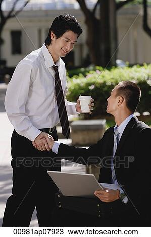 Two men greet each other and shake hands in the park View Large Photo Image Stock Image - Two men greet each other and shake hands in the park. Fotosearch