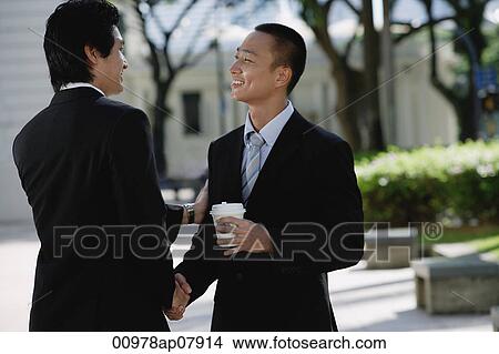Two men wearing suits greet each other and shake hands in the park View Large Photo Image Picture - Two men wearing suits greet each other and shake hands in the park. Fotosearch