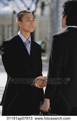 Two men wearing suits greet each other and shake hands in the park View Large Photo Image Stock Image - Two men wearing suits greet each other and shake hands in the park. Fotosearch
