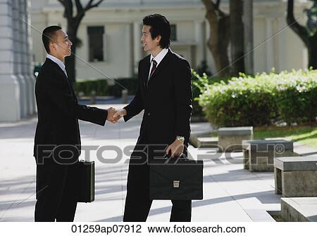 Two men wearing suits greet each other and shake hands in the park View Large Photo Image Stock Image - Two men wearing suits greet each other and shake hands in the park. Fotosearch