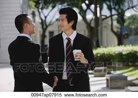 Two men wearing suits greet each other and shake hands in the park View Large Photo Image Stock Photography - Two men wearing suits greet each other and shake hands in the park. Fotosearch