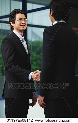 Stock Image - Two men wearing suits shake hands. Fotosearch