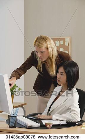 Two woman look at a computer while at work View Large Photo Image Stock Photo - Two woman look at a computer while at work. Fotosearch