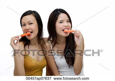 Two young women biting into Popsicle, looking at camera View Large Photo Image Stock Photo - Two young women biting into Popsicle, looking at camera. Fotosearch