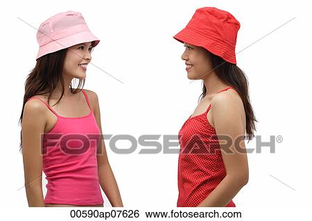 Stock Photograph - Two young women wearing pink and red hats, looking at each other. Fotosearch