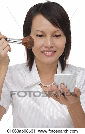 Woman applying cosmetics while looking into compact mirror View Large Photo Image Stock Image - Woman applying cosmetics while looking into compact mirror. Fotosearch