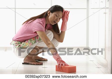 Stock Image - Woman cleaning kitchen floor with big pink sponge, tired. Fotosearch