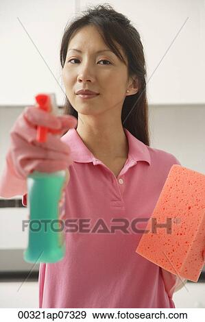 Stock Photo - Woman cleaning with cleaning spray and sponge, spraying at camera. Fotosearch