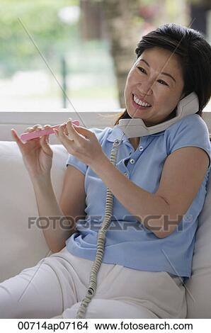 Picture - Woman filing her nails and talking on telephone. Fotosearch