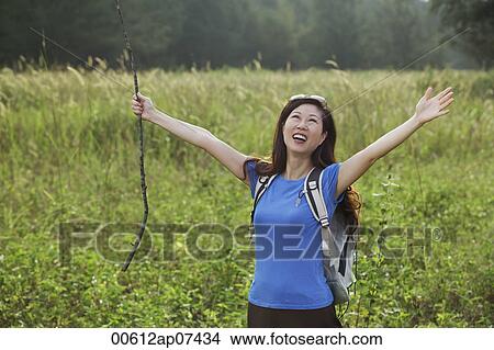 Picture - Woman hiking in nature, raising arms to the sky and smiling. Fotosearch