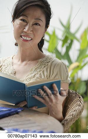 Stock Image - Woman holding a book, smiling at camera. Fotosearch