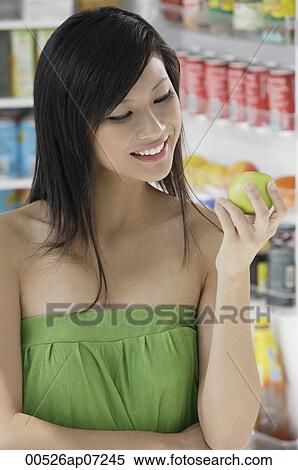 Stock Photography - woman holding apple in front of open refrigerator. Fotosearch